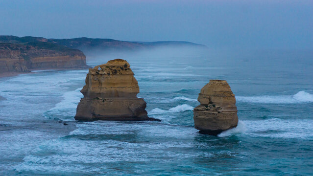 View of rugged limestone stacks rise majestically from the turbulent turquoise sea under a muted sky, a coastal drama unfolding, Twelve Apostles, Victoria, Australia.
