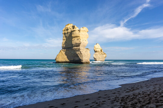 View of majestic limestone stacks rise from the turquoise sea under a bright blue sky, waves crashing gently on the sandy shore, Twelve Apostles, Victoria, Australia.