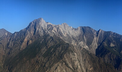 Aerial view of jagged, rocky peaks piercing the clear blue sky, their rugged faces etched with shadows and light, Gilgit, Gilgit Baltistan, Pakistan.