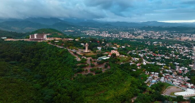 Approaching the Watchman Cross located on the green hill. Scenery of Ponce, Puerto Rico surrounded by mountains covered with grey clouds.