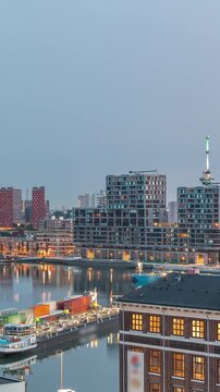 Aerial view over towers in Maashaven night to day transition timelapse with moored ships, Katendrecht and Maas River, Rotterdam before sunrise. Illuminated factory converted to office and event space
