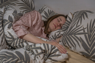 Woman sleeps in bed with patterned sheets and pillows during nighttime