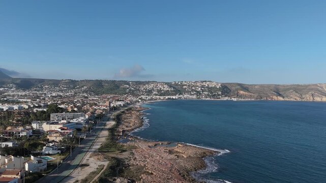 Panoramic drone video of rocky coast with crashing waves, turquoise sea and harbor in background. Javea Alicante Espa&ntilde;a.