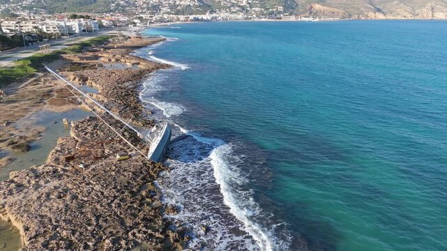 Drone video of a sailboat stranded on coastal rocks during a storm, blue sea visible on a clear day, Javea Alicante Spain.