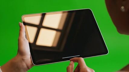 Closeup of a persons hands holding a modern digital tablet with a blank white screen interacting with touch gestures against a vibrant green chroma key background perfect for adding custom content an.