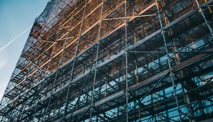 Construction scaffolding against a bright, sunlit sky, highlighting the intricate framework of a building under development and urban renewal projects