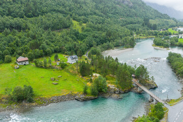 Obraz premium Drone view, aerial view of Romsdalen valley and Rauma river. Bridge over river, lonely house on riverbanks with surrounding meadows. Beautiful valley in western Norway. Pine trees and meadow on the ri