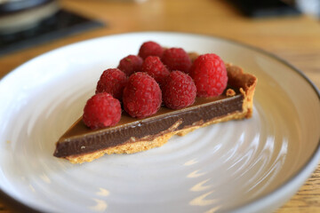 Slice of chocolate tart with fresh raspberry on plate for dessert
