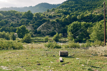 Fototapeta premium Rural landscape with a grassy field, distant hills, a log and a small hay bale, creating a simple peaceful outdoor scene in nature.