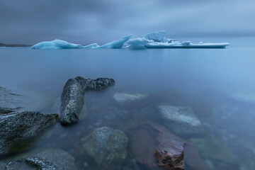 Icebergs drifting near the edge of a glacier lagoon in Iceland, captured with long exposure for smooth water and a cold, minimalist atmosphere. Pristine Arctic landscape and climate concept.