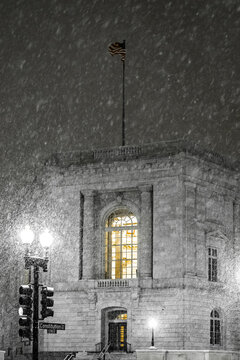 View of a building with a warm, inviting glow emanating from its windows amidst a flurry of snowflakes on a cold winter night, Washington DC, United States.