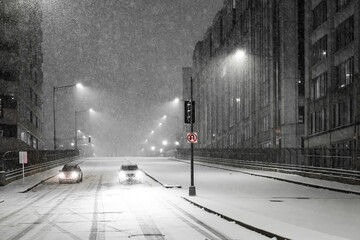 View of a snow-covered street scene with cars moving along the road under the glow of streetlights during a heavy snowfall, Washington DC, United States.