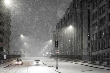 View of a snow-blanketed city street with cars braving the blizzard under the glow of streetlights, creating a stark contrast against the dark buildings, Washington DC, United States.