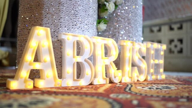 Illuminated marquee letters spelling the name 'ABRISH' on a floor with a silver sequin background for a wedding or birthday event