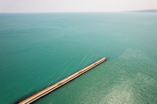 Aerial view of a long pier stretching into the turquoise sea, creating a stark contrast between the man-made structure and the natural expanse, Balchik, Dobrich Province, Bulgaria.