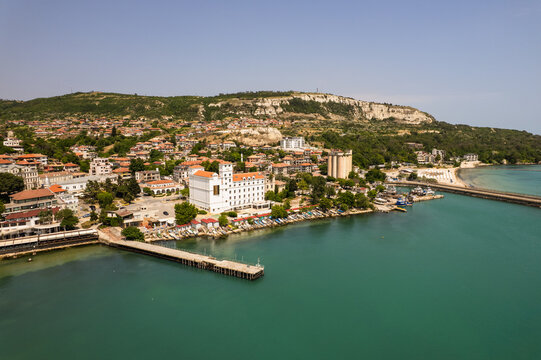 Aerial view of the bright white architecture contrasts against the deep turquoise waters of the harbor, framed by the rugged, verdant cliffs, Balchik, Dobrich Province, Bulgaria.