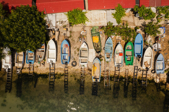 Aerial view of colorful fishing boats line the shore, reflecting in the calm water under the warm sun, near the red-roofed buildings, Balchik, Dobrich Province, Bulgaria.