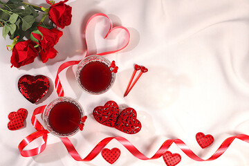 Two glasses of red wine on a festive table with roses, hearts, and a ribbon. Valentine's Day concept, advertising for a bar and cafe. Banner for an invitation to a festive buffet, card for a wedding,