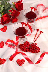 Two glasses of red wine on a festive table with roses, hearts, and a ribbon. Valentine's Day concept, advertising for a bar and cafe. Banner for an invitation to a festive buffet, card for a wedding,