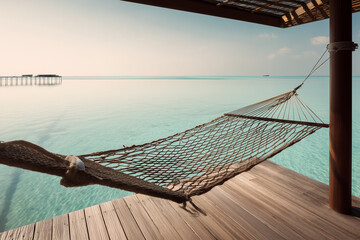 Empty hammock on a wooden deck overlooking calm turquoise ocean water at sunrise.