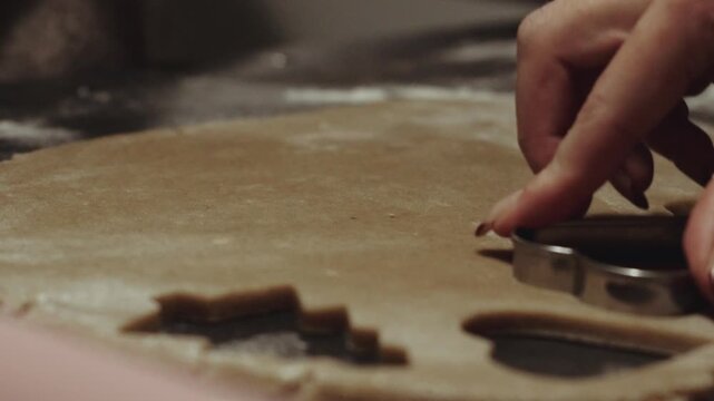 Female baker with christmas nails cutting cookie dough with cookie cutter, making christmas gingerbread cookies during family holyday baking day. Desaturated footage easily color matched
