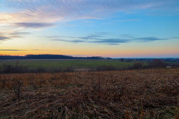 Obraz premium ​A wide autumn field with dry grass unfolds under an endless evening sky where the soft light of sunset meets the deep blue.