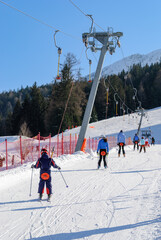 Skiers using a drag lift on a snowy ski slope in the mountains, winter sports scene with people, clear blue sky, alpine resort atmosphere.