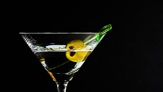 Glass of cocktail with olive on stick against black background in a bar setting with soft lighting