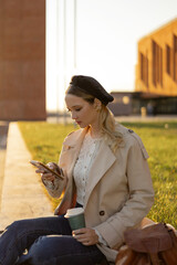 A young girl sits on a green lawn in a park with a smartphone in her hands
