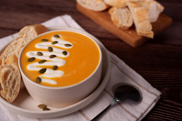 warm and wholesome creamy pumpkin soup with pumpkin seeds and baguette slices on rustic wooden...