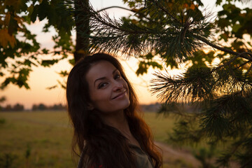 Beautiful woman in a park touching hand and looking on a Christmas green tree with happy smiling in sunset sky light on the street outdoor with copy space nature beautiful background.