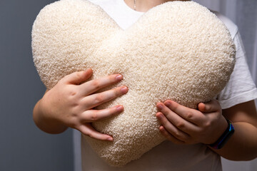Man holding white fluffy heart shaped pillow, close up view, warm and romantic Valentine's Day...