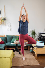 Woman practicing yoga tree pose at home living room