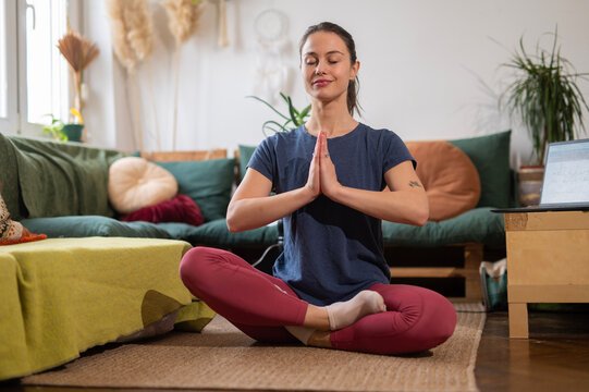 Woman meditating in lotus position practicing yoga at home