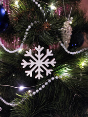 Close-up of white snowflake ornament on artificial Christmas tree with decorations in background