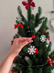 Woman&rsquo;s hand hanging snowflake ornament on artificial Christmas tree