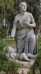 Rome, Italy - 12 January 2025. Villa Borghese Gardens sculpture of a kneeling woman gazing upward beside a child figure in a basin, framed by foliage.
