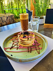Stacked, sweet pancakes with decoration and a frappe, decoratively arranged on a plate