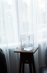 Empty glass vase on wooden stool near window in minimalist interior
