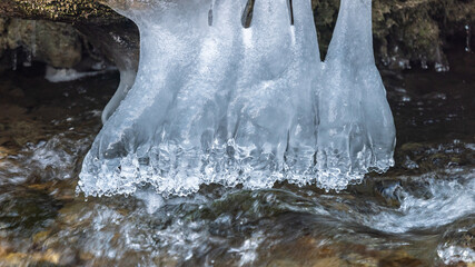 Icy fingers grip the edge, frozen in time above the stream. Winter's art shapes the landscape, a delicate dance of cold and flow. Frozen marvels on display.