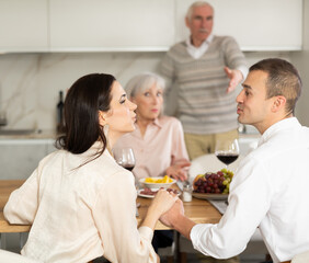 Man and his chosen one are sitting at table during family feast with elderly parents. Mature couple looks accusingly at their son and his girlfriend.