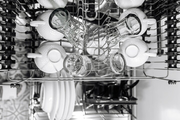 Dishwasher interior filled with clean white dishes, glasses, and cups arranged neatly, showcasing...