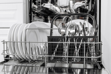 Dishwasher interior showcasing neatly arranged plates and utensils in a black basket, highlighting cleanliness and organization in modern kitchen appliances with copy space