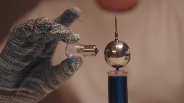 Close-up of scientist performing science experiment, wirelessly illuminating light bulb with electromagnetic field generated by high frequency coil, researching electrical energy, plasma technology.