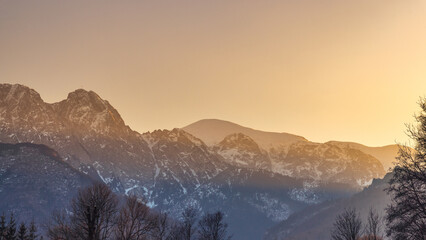 Giewont peak in Tatra Mountains above Zakopane town in Poland, Europe. An ethereal landscape with the snowy mountains rising beneath a sun-kissed sky at early morning or late afternoon.