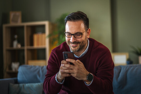 Smiling man using smart phone browsing social media at home