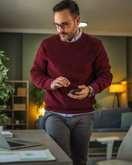 Man standing at home office checking smart phone