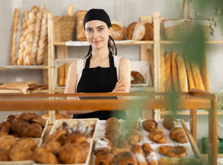 Young female salesperson at showcase with fresh pastries in bakery