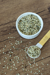 Hemp seeds in a dish and spoon on wooden table.