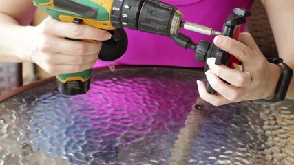 Woman using a cordless power screwdriver to remove a screw from a plastic phone holder. Horizontal video ideal for diy repair, small device maintenance and power tool tutorial content.